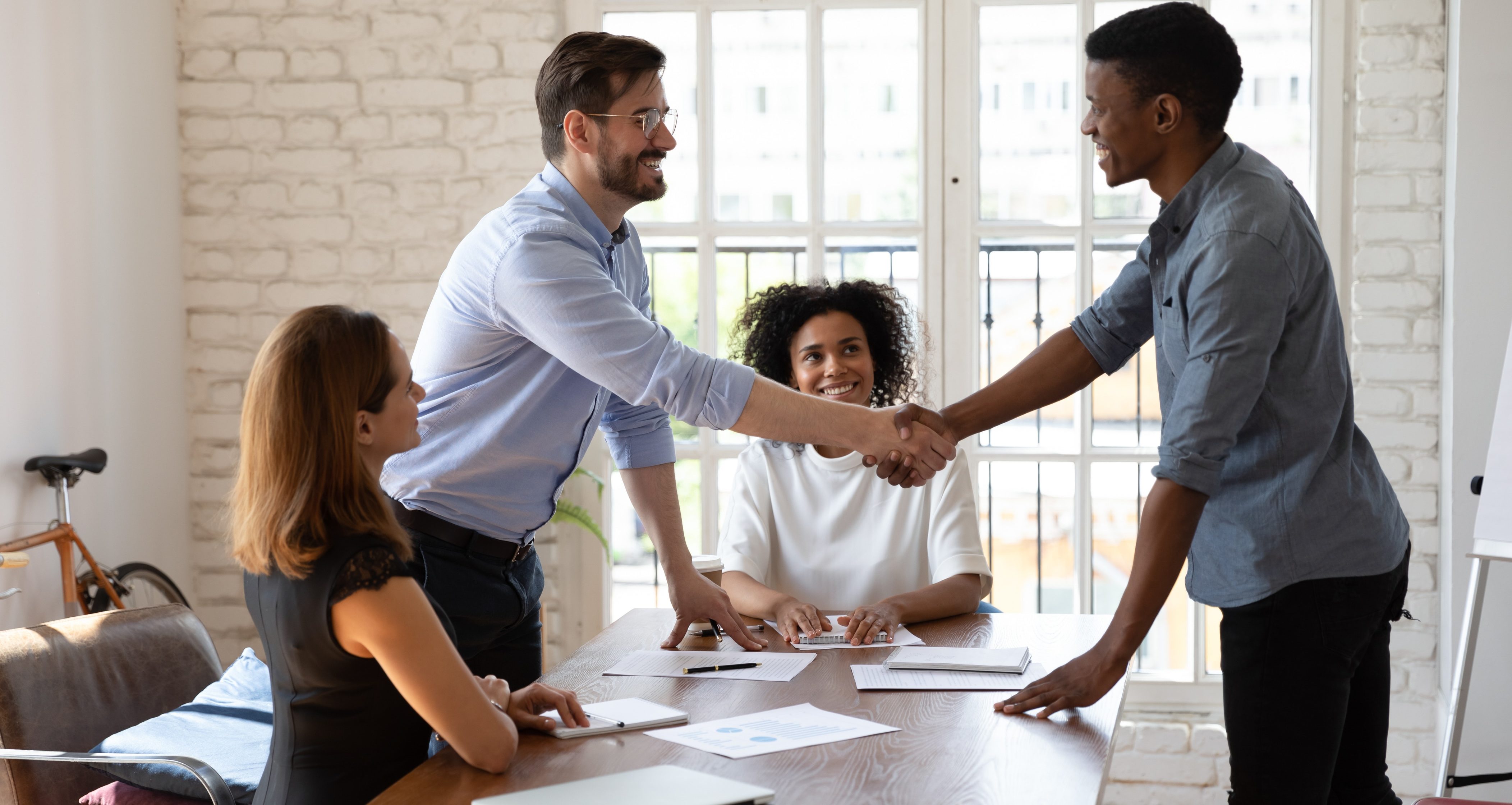 Smiling multiethnic male employees shake hands greet get acquainted at office meeting, happy diverse multiracial coworkers colleagues handshake congratulate with promotion close deal at briefing